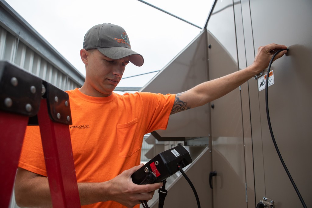 man holding a piece of equipment into an HVAC unit