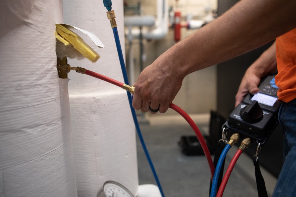 man testing ductwork by putting a red cable through a small opening in the insulation of the ductwork